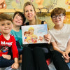 Die Mutter hält ihr kostbares Geschenk in der Hand, ein Buch mit individuellen Figuren von ihr und ihren drei Kindern.	