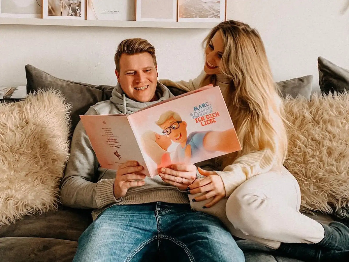 Mann und Frau sitzen auf einer Couch und halten ein personalisiertes Buch der Liebe in der Hand.	