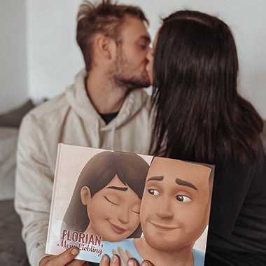 Eine Frau küsst ihren Freund, der ein personalisiertes Buch für Paare in der Hand hält, das perfekte Geschenk für den Freund.