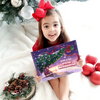 Kind sitzt vor einem Weihnachtsbaum und hält das personalisierte Buch „Jasmin & Papa – Erstes Weihnachten 2025“.